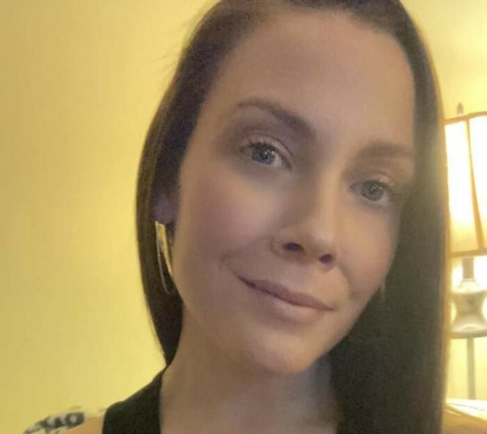 Mujer con cabello largo y aretes oscuros en una habitación suavemente iluminada, relacionada con la acción escolar contra el incidente del jugador de fútbol.