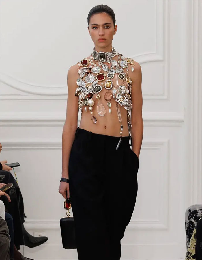 Modelo con un top con adornos y pantalones negros adornados con vanguardia, destacando las ideas estilistas de Jenna Ortega sobre el atuendo viral del Emmy.