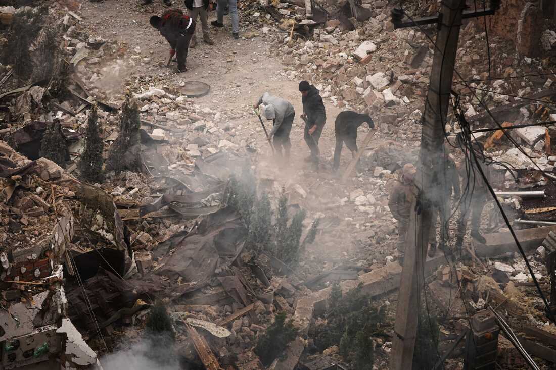La gente despeja los escombros en el sitio de los edificios de apartamentos dañados durante un ataque ruso en Kiev el domingo.