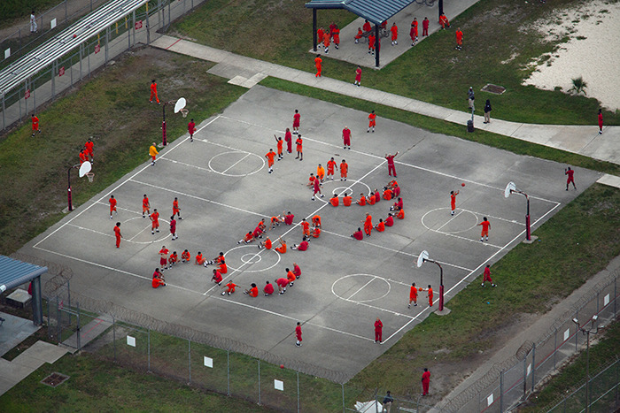 Vista aérea de los detenidos con uniformes de naranja reunidos en una cancha de baloncesto al aire libre en un centro de detención de hielo.