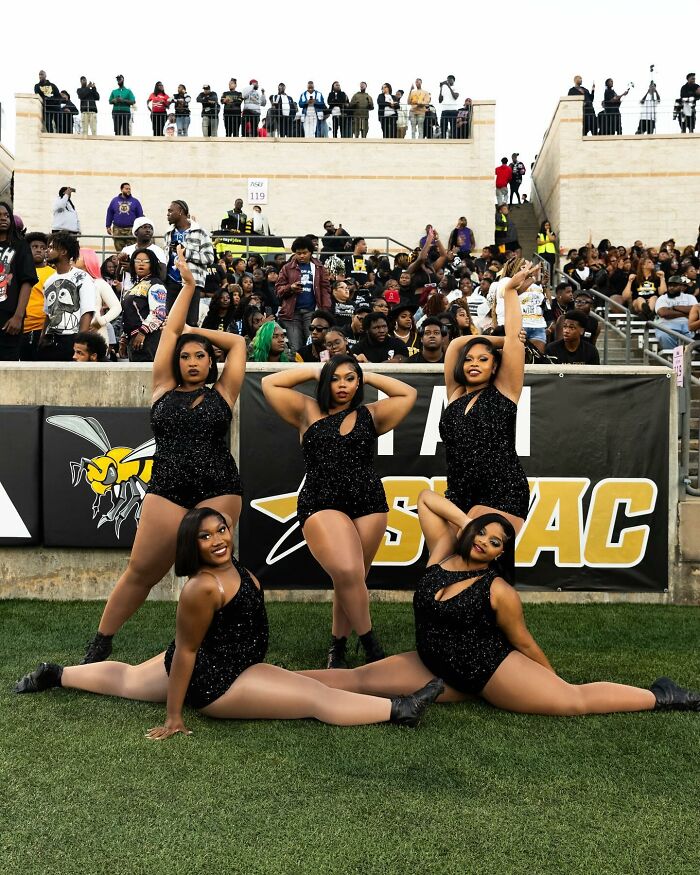 Los bailarines de la banda universitaria se presentan en el medio tiempo con trajes negros con una multitud en el estadio, destacando la representación de talla grande.