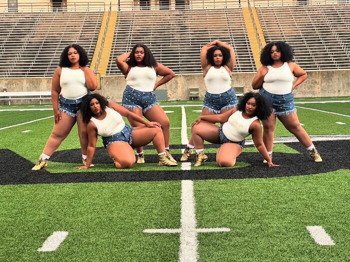 Los bailarines de talla grande actúan con confianza en el campo de fútbol durante el medio tiempo, mostrando movimientos audaces a pesar de la reacción de la banda de la banda universitaria.