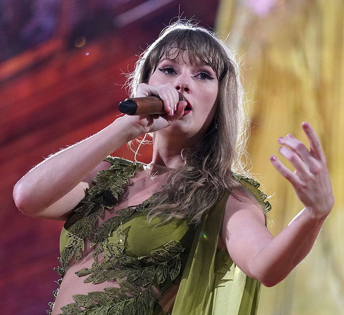 Taylor Swift actuando en el escenario con atuendo verde, provocando una reacción violenta sobre letras filtradas de la vida de una showgirl.