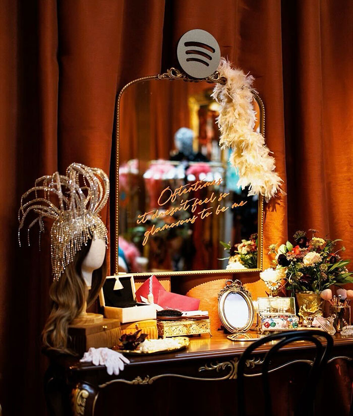 Mesa de tocador con tadro de showgirl emplumado, decoración vintage y un espejo con letras que reflejan la reacción de tono de tono sordo taylor swift.