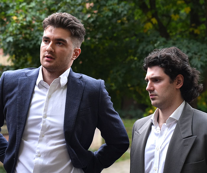 Dos hombres con trajes al aire libre, que parecen serios mientras discuten los hallazgos forense sobre la influencia del rechazo de quimioterapia.