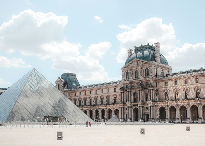 Exterior del Museo del Louvre con entrada en forma de pirámide de cristal bajo un cielo azul, que hace referencia al famoso ladrón de joyas y trucos de contrabando.
