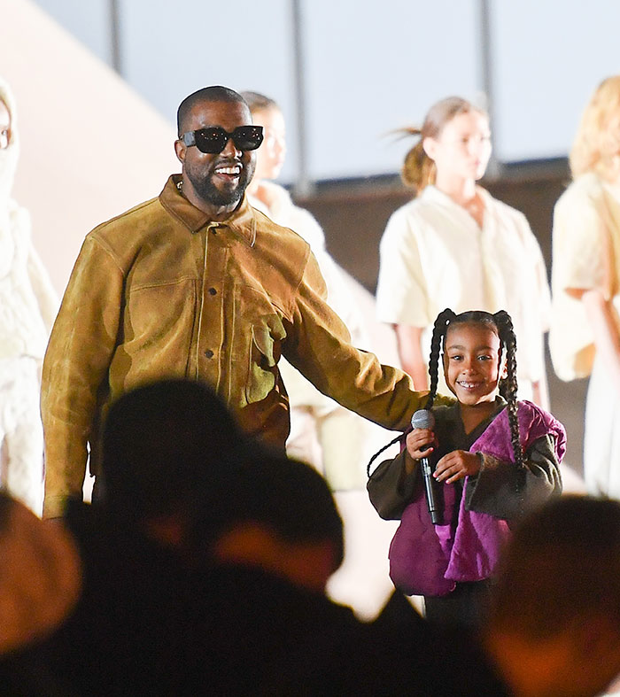 Kanye West de pie con su hija North West sosteniendo un micrófono durante un evento público en medio de preocupaciones sobre la vida en línea.