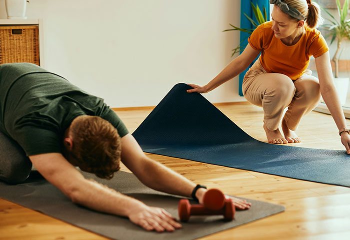 Pareja practicando yoga sobre colchonetas en casa, destacando la tensión y los desafíos en su matrimonio durante actividades compartidas.
