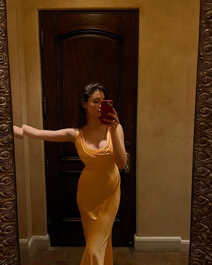 Mujer tomándose un selfie en el espejo con un vestido vintage amarillo, mostrando elegancia atemporal y moda clásica en un evento de gala.
