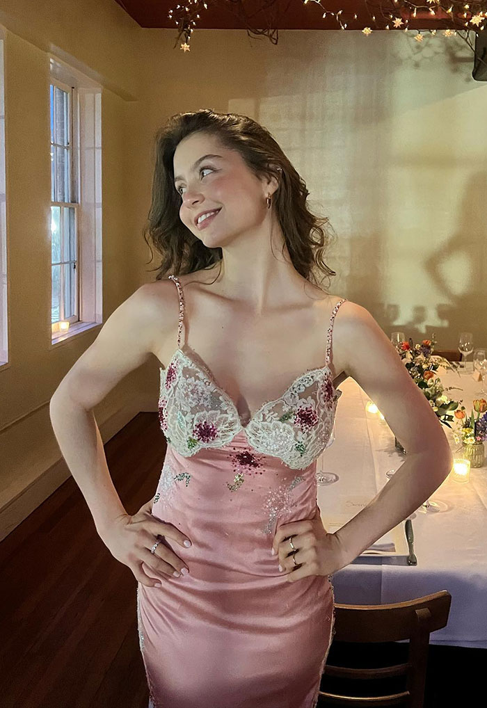Mujer joven con un vestido floral rosa vintage, sonriendo y posando en una habitación suavemente iluminada en un elegante evento de gala.