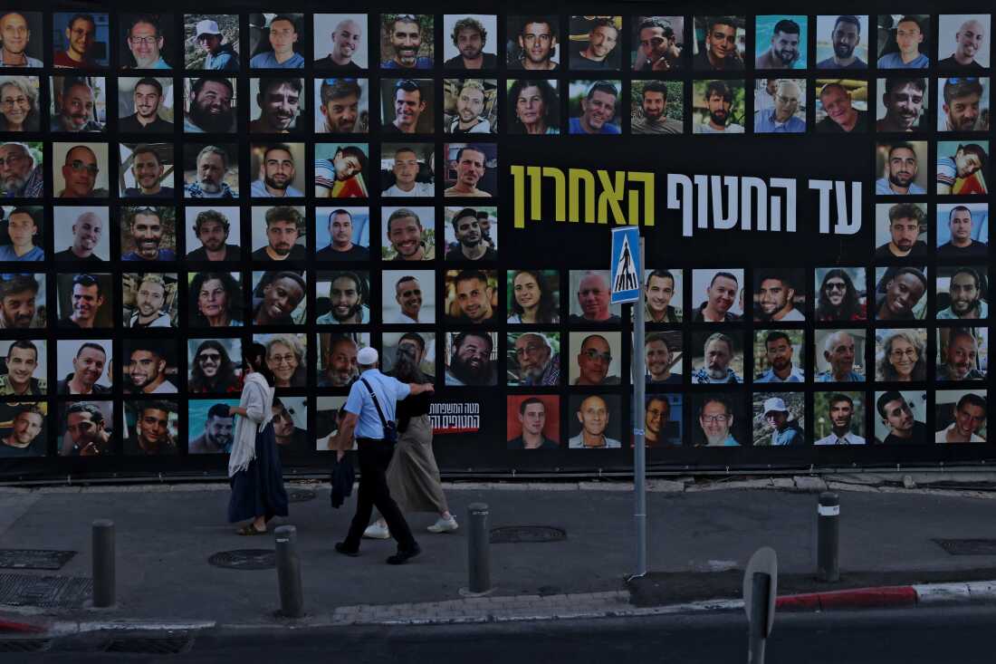 La gente pasa junto a un cartel con retratos de israelíes retenidos como rehenes en la Franja de Gaza por militantes palestinos desde 2023, en Jerusalén el 6 de octubre de 2025.