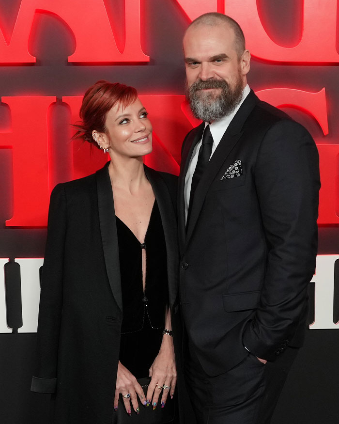 David Harbour y el coprotagonista de Stranger Things sonríen en el evento con el telón de fondo rojo de Stranger Things detrás de ellos.