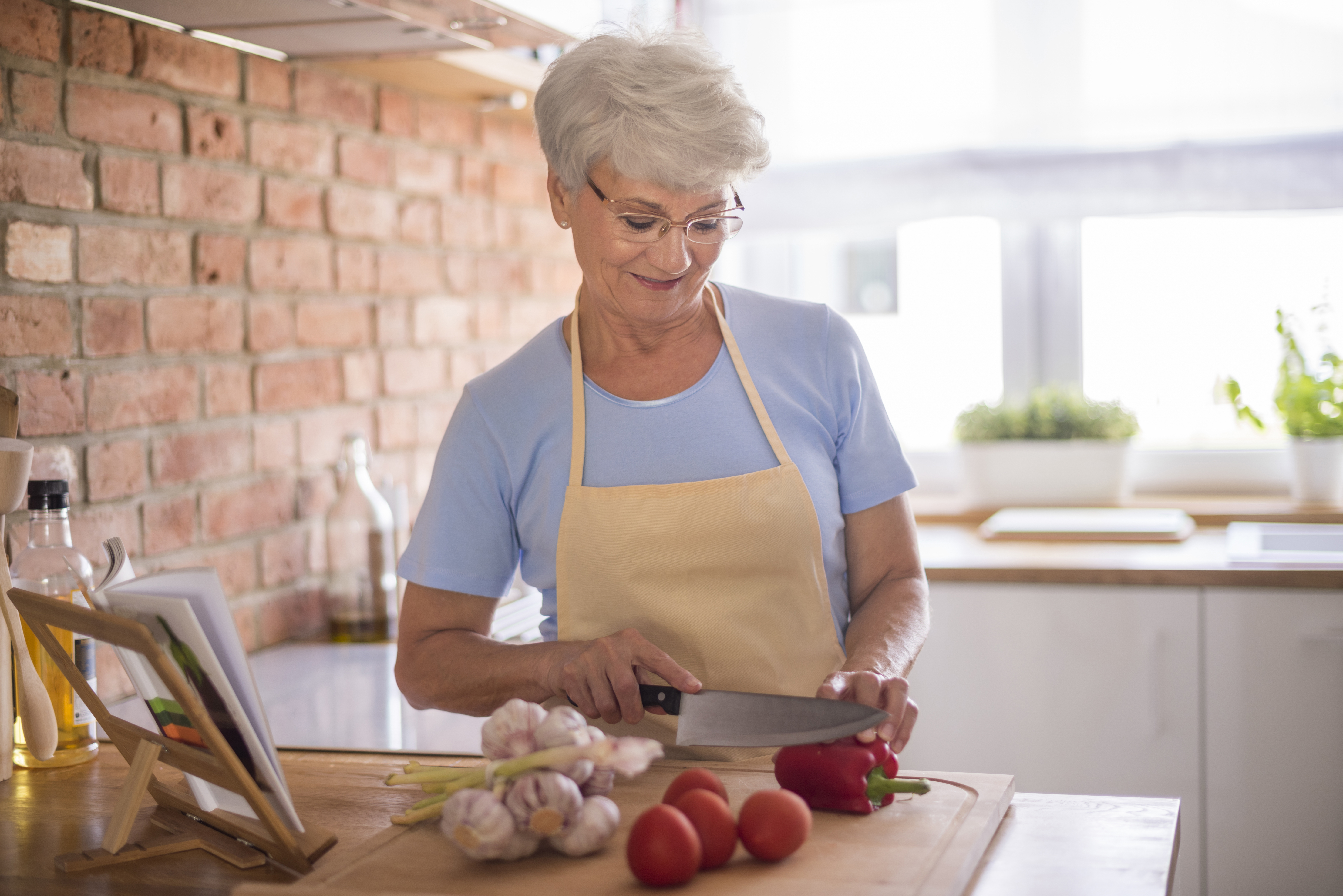 Mujer mayor preparando verduras en una cocina, lo que ilustra las preocupaciones culinarias de MIL que afectan los planes de Acción de Gracias de las mujeres embarazadas.