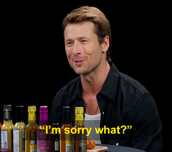 Glen Powell durante una entrevista con varias botellas de salsa picante, destacando un momento viral de error de Hollywood.