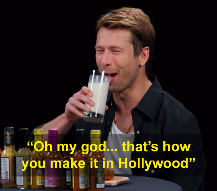 Glen Powell durante el error de una entrevista viral, sosteniendo un vaso de leche, destacando la exposición al lado oscuro de Hollywood.