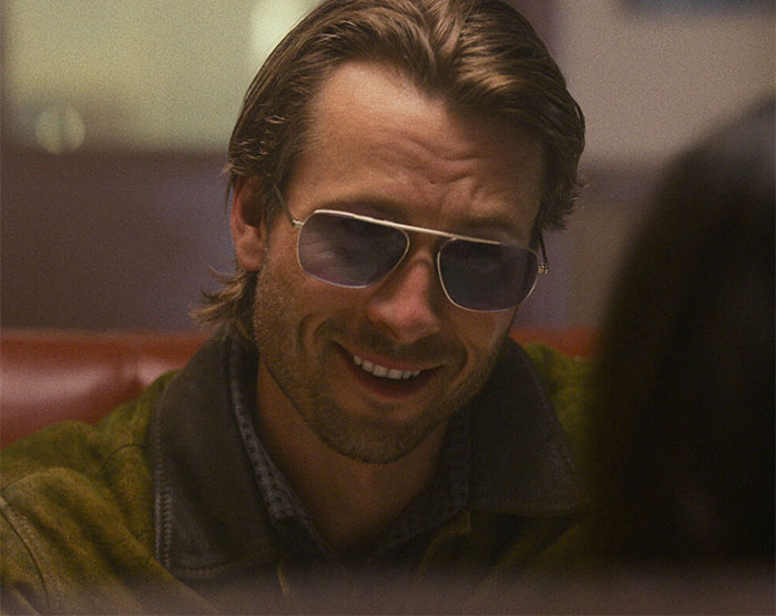 Glen Powell con gafas de sol y sonriendo durante una entrevista, destacando el error viral y el lado oscuro de Hollywood.