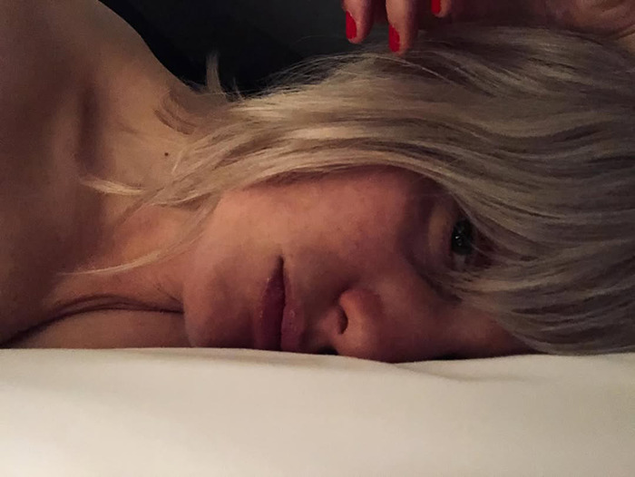 Alison Sudol acostada con cabello rubio, mostrando una expresión contemplativa en un ambiente con poca luz.