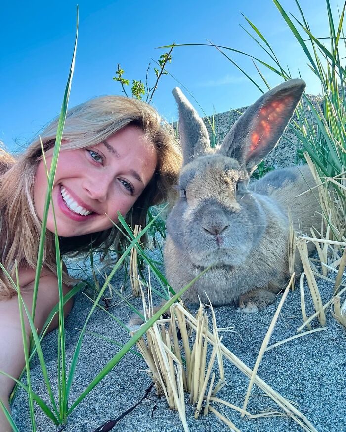 Mujer joven sonriendo junto al conejo Hoppy Gilmore al aire libre, mostrando su naturaleza afectuosa y de compañero canino.