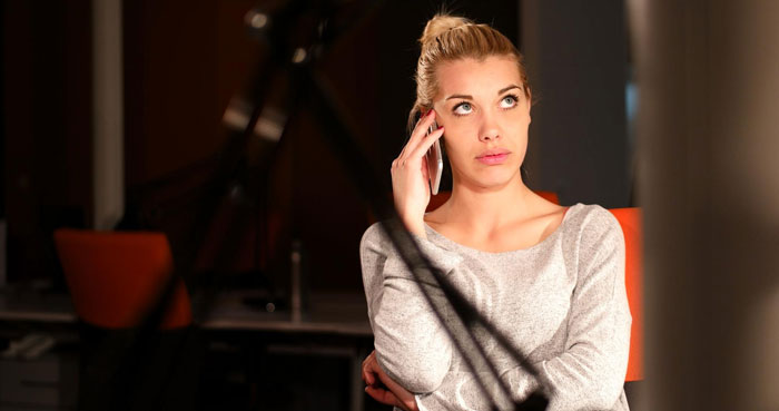 Mujer poliamorosa haciendo una insinuación por teléfono, luciendo frustrada en el interior, capturando la tensión en un ambiente moderno.