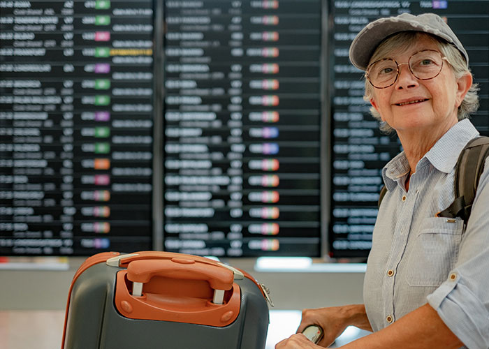 Una anciana con gafas y gorra esperando en el aeropuerto, pareciendo abrumada mientras cuida a varios niños.