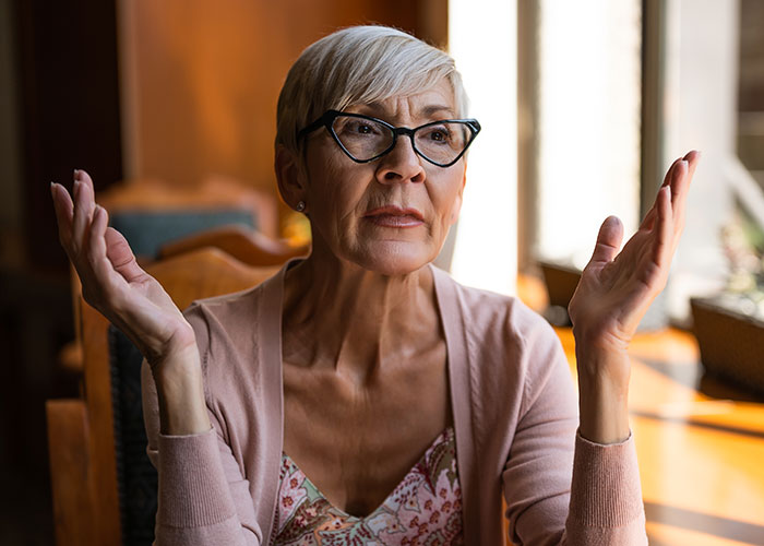 Mujer mayor con gafas que parece frustrada y abrumada mientras cuida a cinco niños en una sala de estar luminosa.