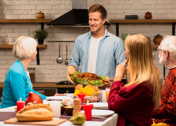 Hombre llevando la cena de Acción de Gracias a su familia sentada a la mesa después de un largo turno de 12 horas, mostrando que mil espera la cena de Acción de Gracias.