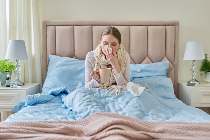 Mujer enferma en la cama sosteniendo una taza, simbolizando la tensión emocional cuando el hombre prioriza el trabajo sobre la vida familiar.