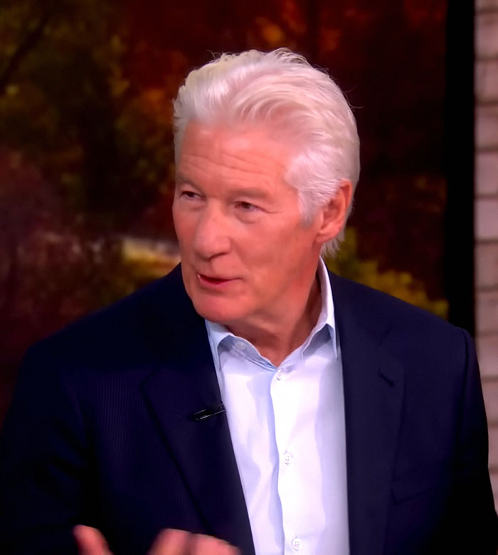 Richard Gere habla en una entrevista, vestido con una chaqueta oscura y una camisa azul claro, sobre la controversia sobre la prohibición de los Oscar.