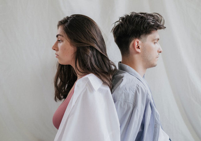 Una mujer joven y un hombre sentados espalda con espalda, resaltando la tensión familiar ya que la mujer no ve los esfuerzos de su hija.