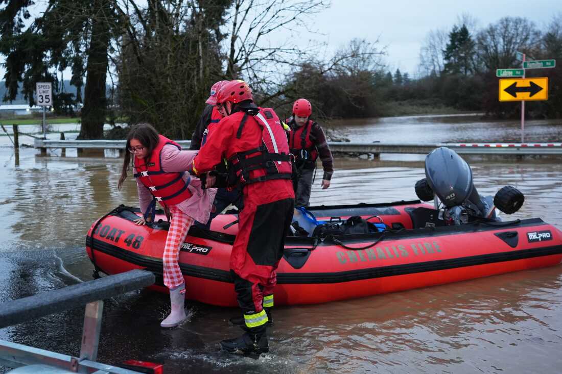 Maery Schine, de 11 años, recibe ayuda de trabajadores de rescate de Chehalis Fire para salir de un bote de rescate después de evacuar con su padre Patric, segundo desde la izquierda, luego de una inundación en Chehalis, Washington, el martes.