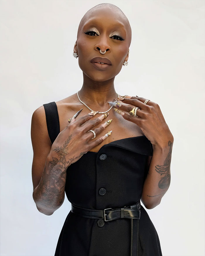 Cynthia Erivo posando con anillos elaborados y uñas cuidadas, resaltando sus manos extrañamente grandes con un vestido negro.