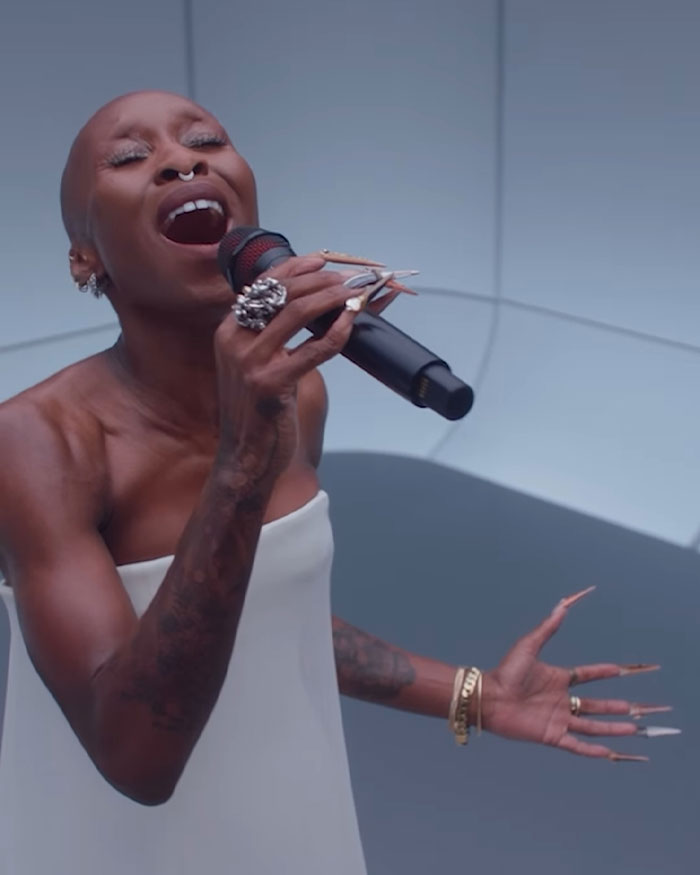 Cynthia Erivo canta apasionadamente con un vestido blanco, destacando sus manos extrañamente grandes y sus largas uñas en una actuación.