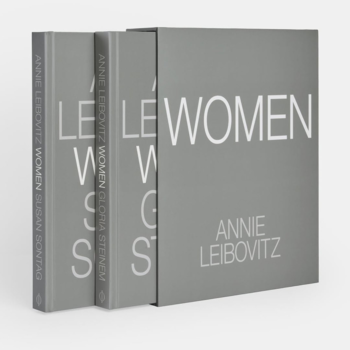 Libros de fotografía apilados de Annie Leibovitz Women con cubiertas grises sobre una superficie blanca que resaltan el nuevo y atrevido tributo al maquillador.