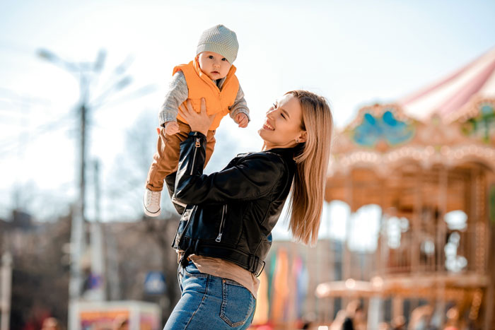 Mamá sosteniendo a un bebé en un parque de diversiones destacando el sueño de Disney con la familia y el costo de la deuda y la culpa que implica