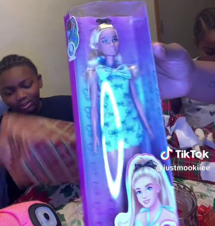Un niño abre los regalos de Angel Tree y muestra su reacción ante un muñeco de juguete mientras su madre graba un vídeo de TikTok.