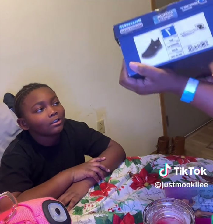 Niño sentado en una mesa con adornos navideños, reaccionando a los regalos de Angel Tree mostrados por una mano adulta.