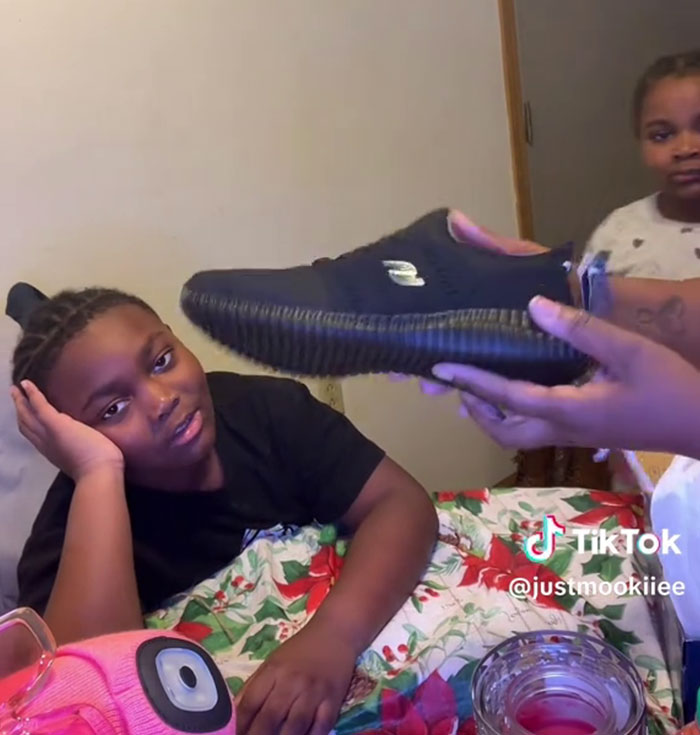 Un niño muestra una reacción ingrata a los regalos de Angel Tree mientras una mujer le tiende un zapato durante un momento familiar filmado en TikTok.