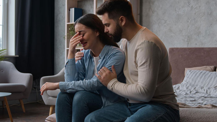 Mujer joven sentada molesta mientras el hombre la consuela en el interior, ilustrando los desafíos de hockey de los niños de la hermana niñera.