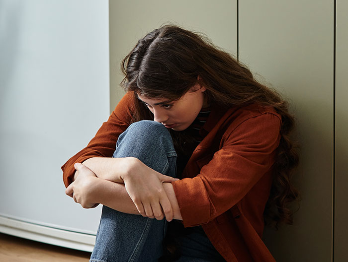 Mujer triste abrazada a las rodillas en el suelo, representando a una madre, toma a su bebé y se marcha furiosa después de una disputa por alimentación con MIL