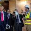 Esta foto muestra al presidente Trump, al presidente de la Reserva Federal, Jerome Powell, y al director de la Oficina de Administración y Presupuesto, Russell Vought, durante una gira de renovaciones en la Reserva Federal en Washington, DC. Powell habla con el gerente de construcción, que lleva un chaleco fluorescente. Los tablones de madera cubren muchas zonas del edificio.
