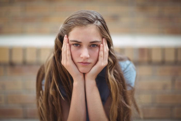 Adolescente con el pelo largo descansando su rostro entre las manos, pareciendo pensativa en un entorno relacionado con el fondo fiduciario de su hijastra.