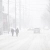 Dos individuos caminan por una calle; ellos, los vehículos detrás de ellos y el edificio junto a ellos están borrosos por la nevada.