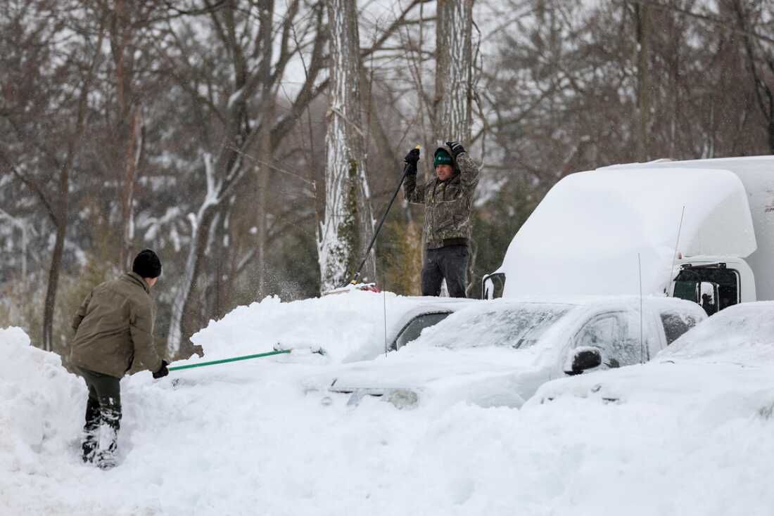 Hombres limpian la nieve de automóviles y camiones el lunes en un estacionamiento en St. James, Nueva York.