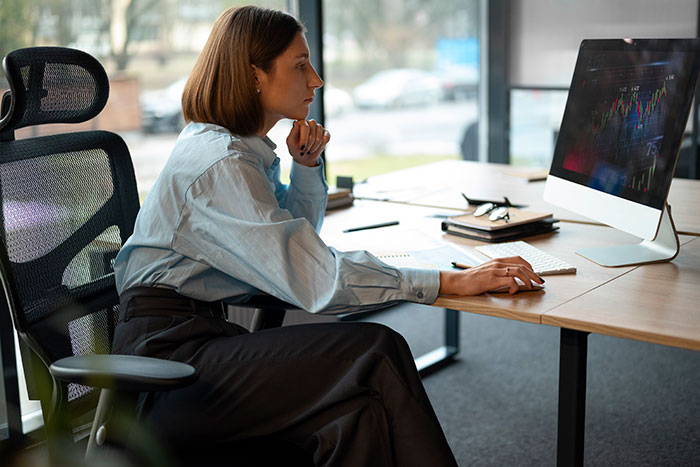 Mujer sentada en un escritorio, mirando pensativamente la pantalla de la computadora, ilustrando conceptos de estándares de belleza y su impacto en las mujeres.