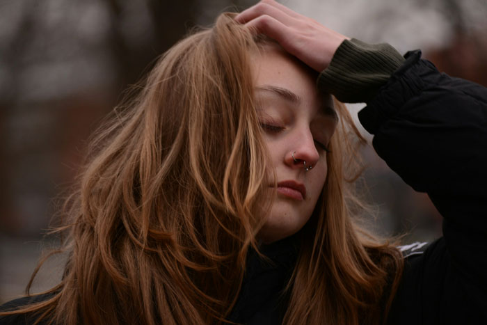Mujer joven con anillos en la nariz tocándose el cabello, mirando pensativa al aire libre, expresando sentimientos sobre mudarse y problemas con el apartamento.