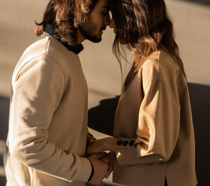 Una pareja joven tomándose de la mano y tocándose la frente, representando a un hombre que quiere mudarse con su novia pero rechaza su apartamento.