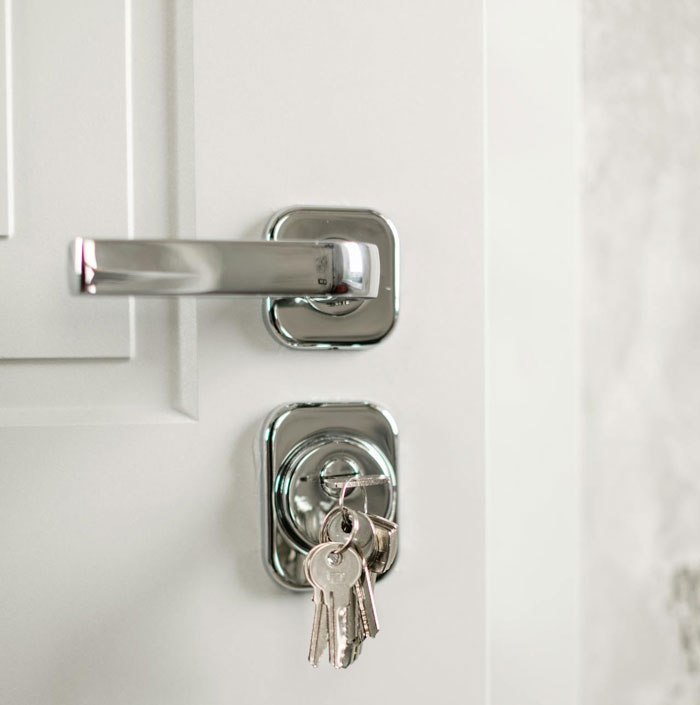 Primer plano del tirador de una puerta con llaves en la cerradura, que simboliza a una mujer harta de ser el portero personal de sus compañeras de cuarto.