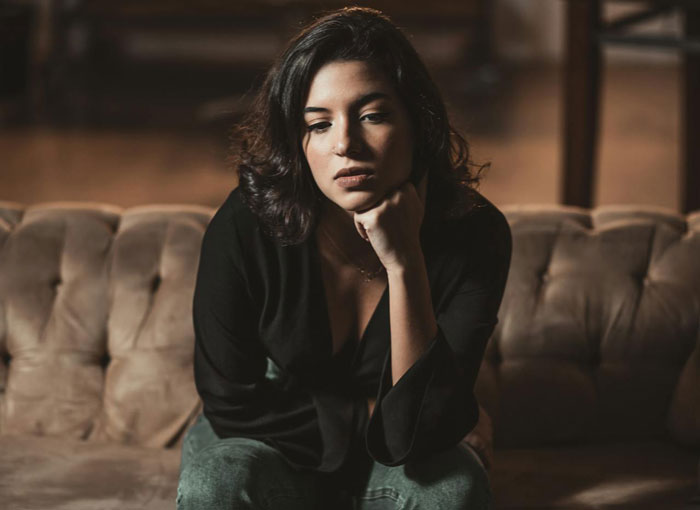 Mujer joven harta de ser el portero personal de sus compañeros de cuarto, sentada en el sofá luciendo frustrada e ignorando las llamadas.