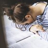 Una estudiante parece fatigada mientras estudia tarde en la noche, apoyando su cabeza en un libro de texto con notas esparcidas, lo que refleja la presión de las exigencias académicas.