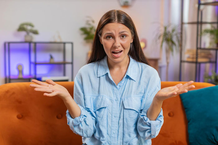 Mujer joven con una camisa azul sentada en un sofá que parece confundida por un problema de relación grosera con un bebé en el interior